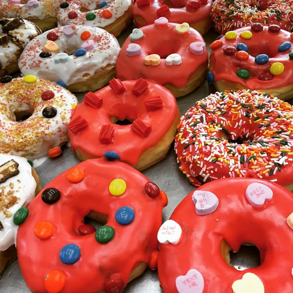 A tray of red-glazed donuts topped with M&Ms, candy hearts, and rainbow sprinkles